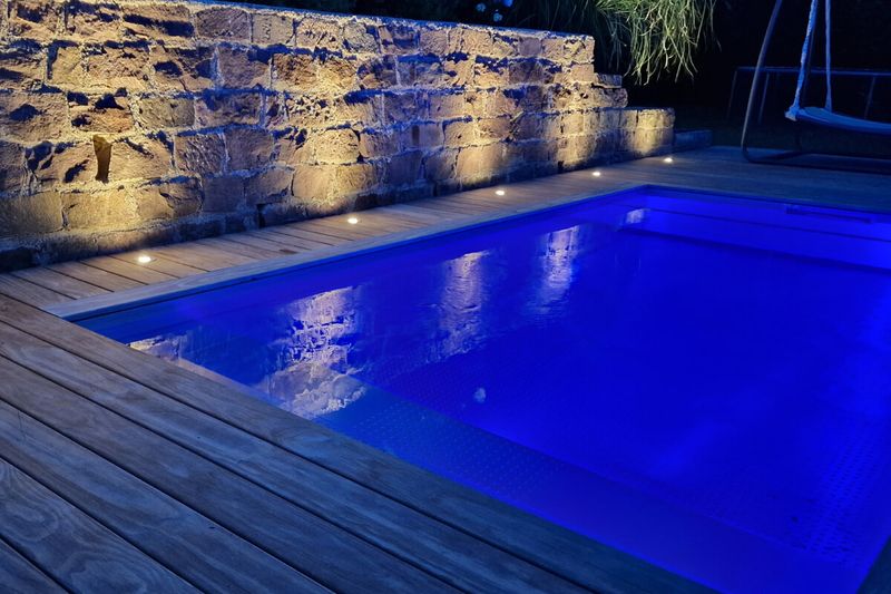 Edelstahlbecken bei Nacht mit blauer LED-Beleuchtung vor einer Steinmauer